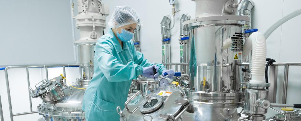 Pharmaceutical factory woman worker in protective clothing operating production line in sterile environment