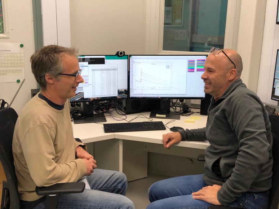 Two men sitting in front of computer monitors 